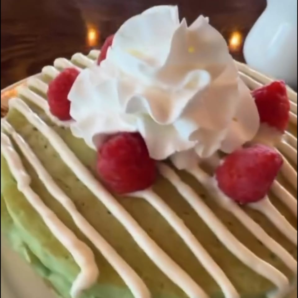 Green pancakes drizzled with white icing, topped with whipped cream and fresh raspberries.
