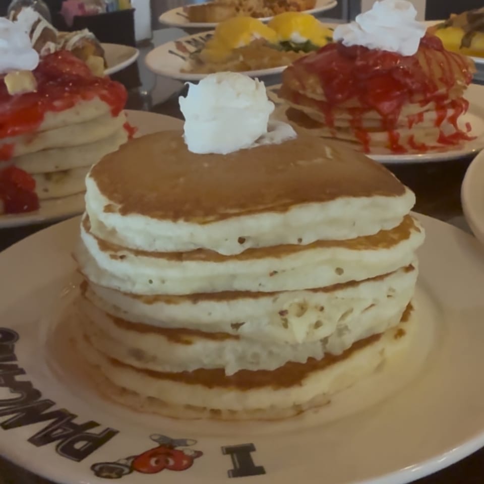 A stack of I Heart Pancakes' golden pancakes topped with a dollop of whipped cream.